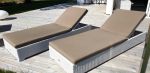 Hagemøbler i hvit rotting som består av to solsenger med brune puter som står ute på en uteplass ved et hvit hus. SparMax